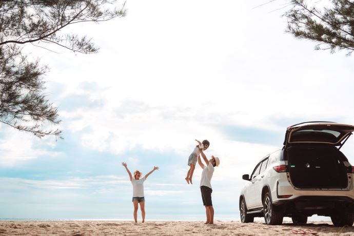 glad familie fjoller foran hvid bil på en strand i udlandet