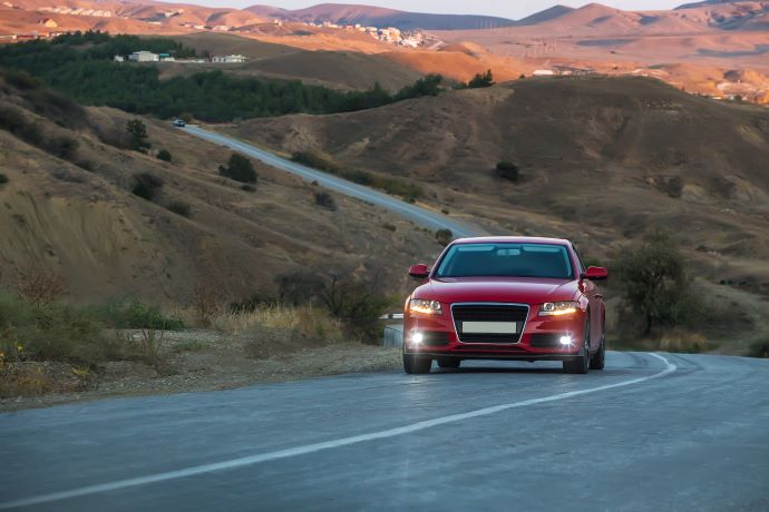 rød bil kører på landeveje med bjerge i solnedgangen