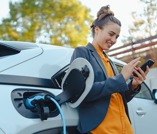 kvinde oplader elbil og ser på mobil