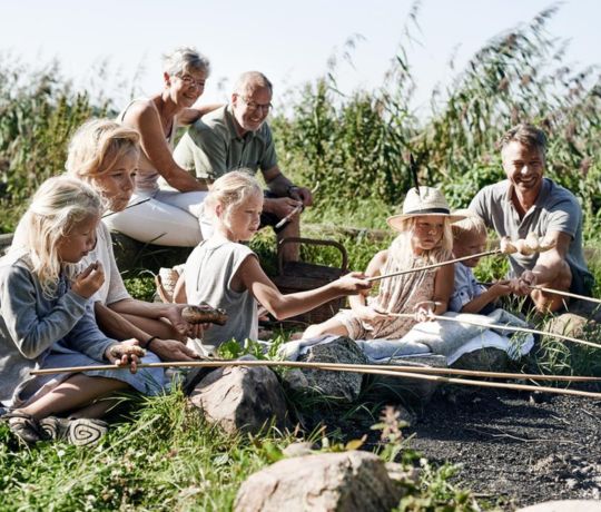 Familie hygger med snobrød på en strand i den danske sommer