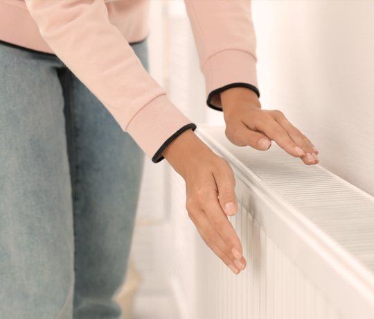 Kvinde varmer sine hænder på en radiator med naturgas fra DCC Energi