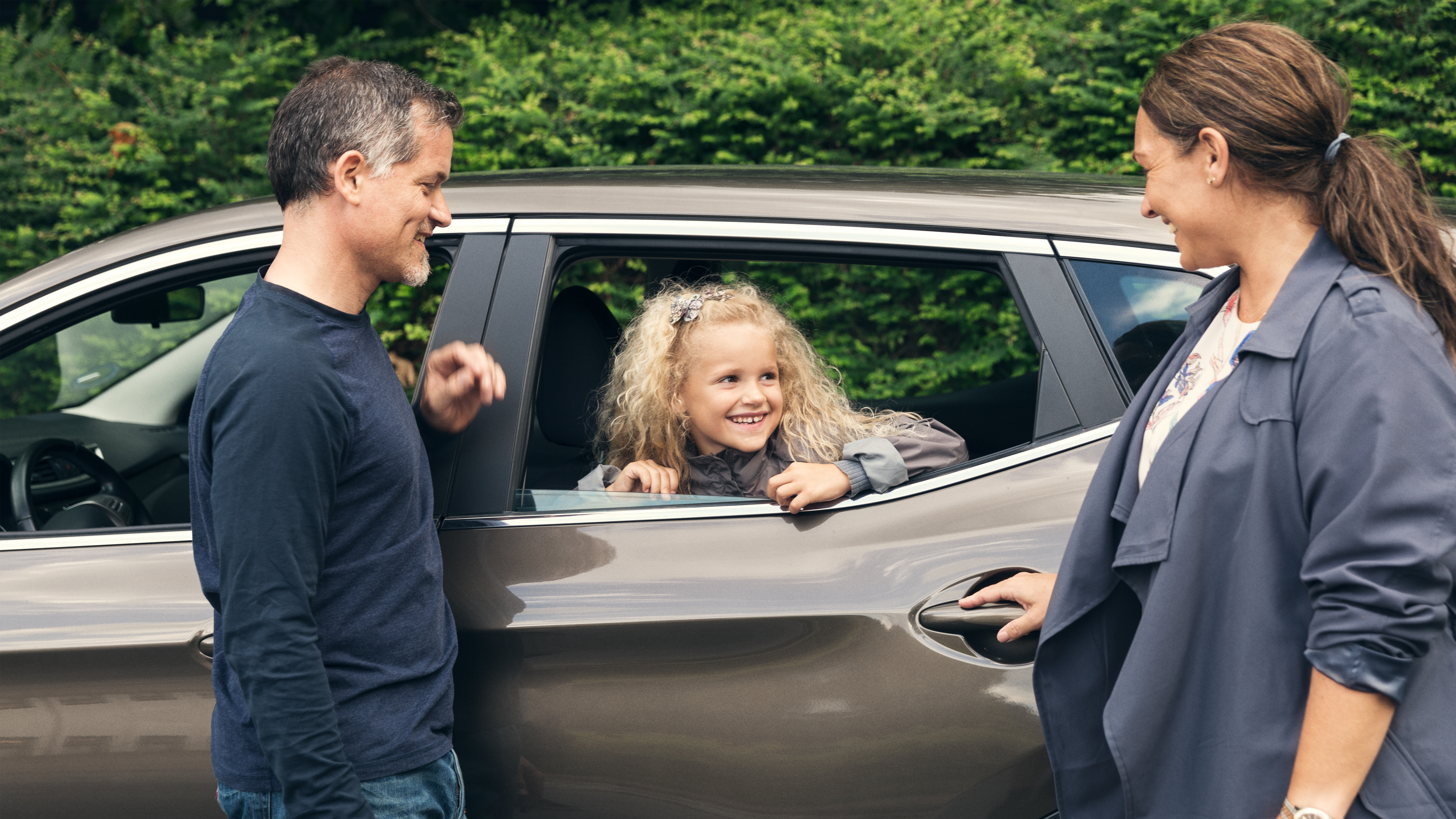 familie smiler til hinanden ved en brun bil
