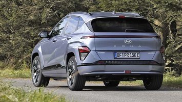 En koksfarvet Hyundai Kona set bagfra, mens den kører på en vej med træer i baggrunden