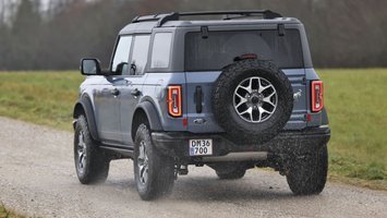 En Ford Bronco set bagfra, mens den kører på en landevej med græs i baggrunden.