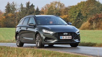 En sort Hyundai i30 stationcar set forfra, mens den kører på en landevej med græs i baggrunden