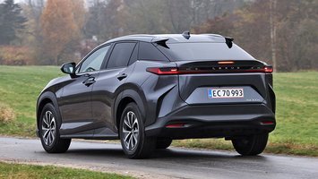 Lexus RZ set bagfra, mens den kører på landevej med græs rundt om