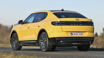 Gul Ford Capri set bagfra, mens den kører på en landevej med græs i forgrunden