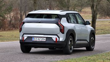Kia EV3 set skråt bagfra, mens den kører mellem træer på en vej