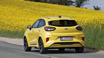 Gul Ford Puma set bagfra, mens den kører på vej med rapsmarker i baggrunden