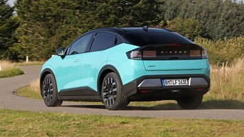 Nissan Leaf set bagfra, mens den kører på landevej med træer i baggrunden