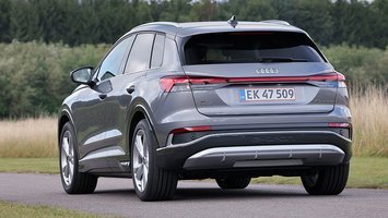 Audi Q4 e-tron set bagfra, mens den kører på landevej med træer i baggrunden.