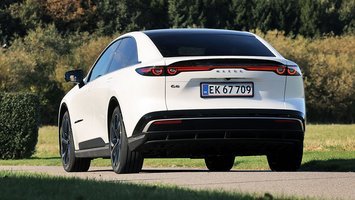 Mazda 6e set bagfra, mens den kører på en landevej med træer i baggrunden