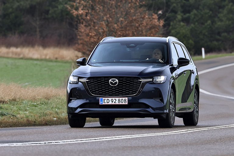 Mazda CX-80 set forfra, mens den kører ud af sving på landevej