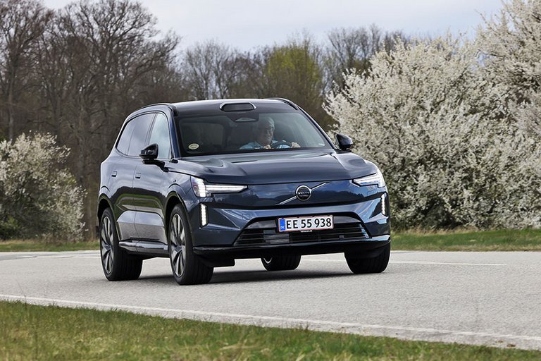Volvo EX90 set forfra, mens den kører på vej med blomstrende træer i baggrunden