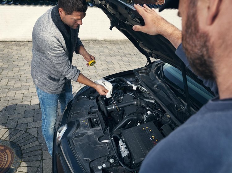 Mand kontrollerer olien på sin bil udenfor. 