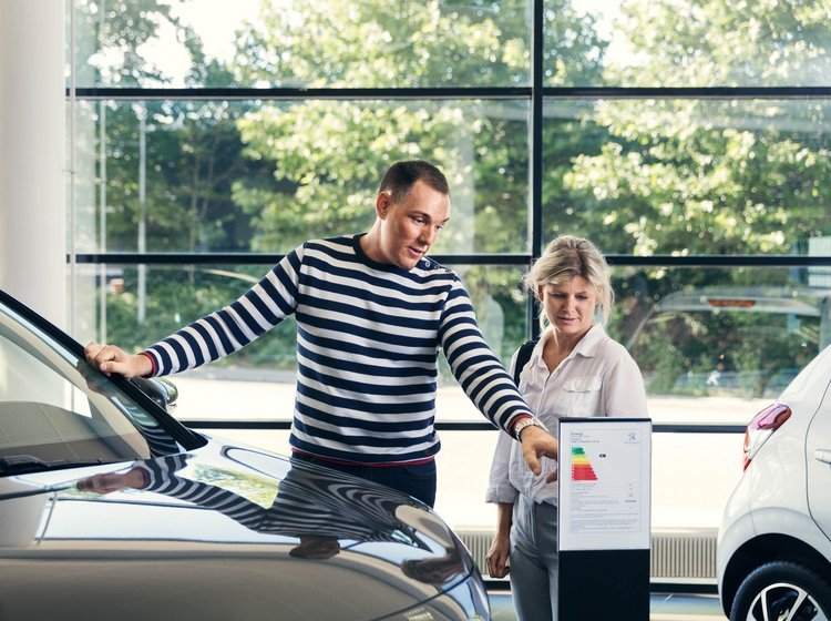 Mand og kvinde overvejer at lease en bil og står i butikken hos en bilforhandler. 