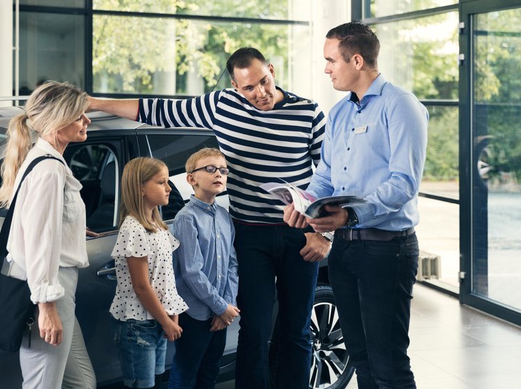 Familie i butik, som sælger biler. Bilsælger viser et katalog frem for familien. 