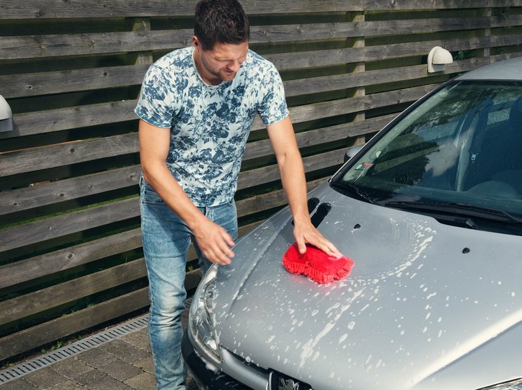 Mand er ved at vaske kølerhjelmen på sin bil. 