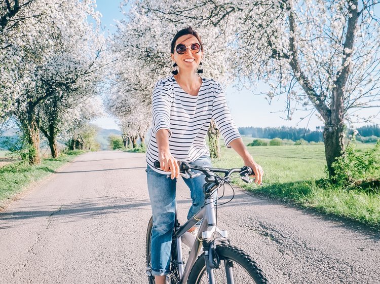 Kvinde på cykel, der kører under blomstrende æbletræer