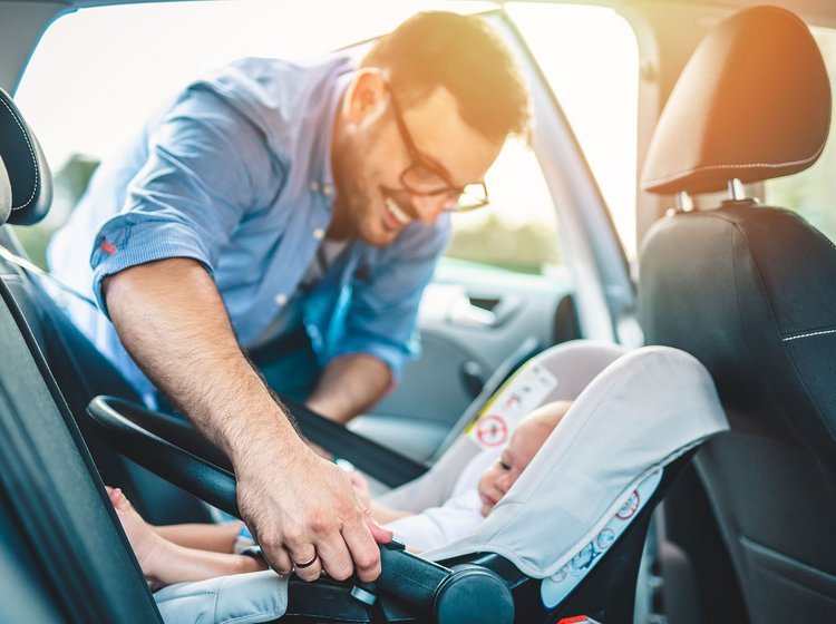 Mand sætter barn i autostol i sin bil.