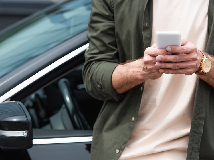 Mand står foran bil og kigger på sin mobil. 