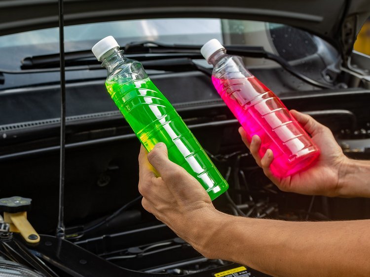 To flasker med kølervæske i forskellige farver foran motor på bil.  