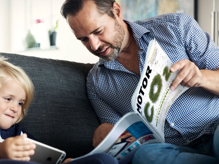 Mand og barn læser magasinet Motor i en sofa