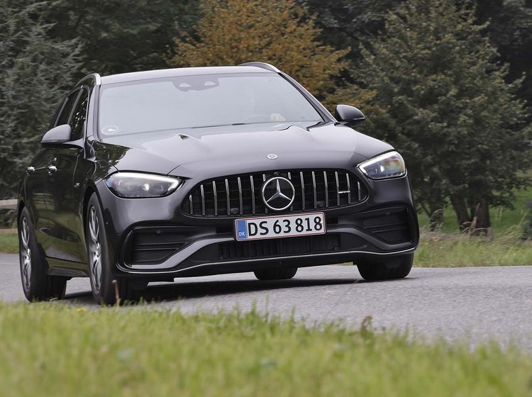 En sort Mercedes C 43 AMG kører i et sving på en landevej med træer i baggrunden.