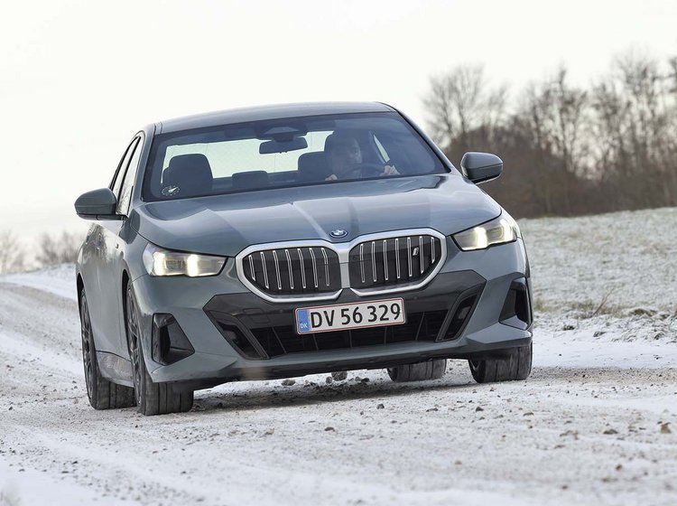 En BMW i5 elbil set forfra kører på en snedækket vej i et snedækket landskab.