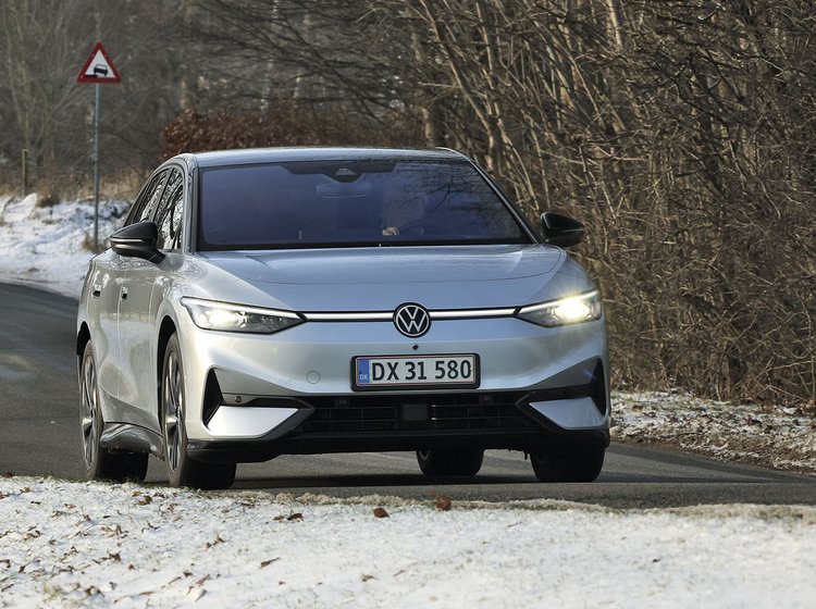 En sølvgrå VW ID.7 kører på en landevej med sne i forgrunden og træer i baggrunden