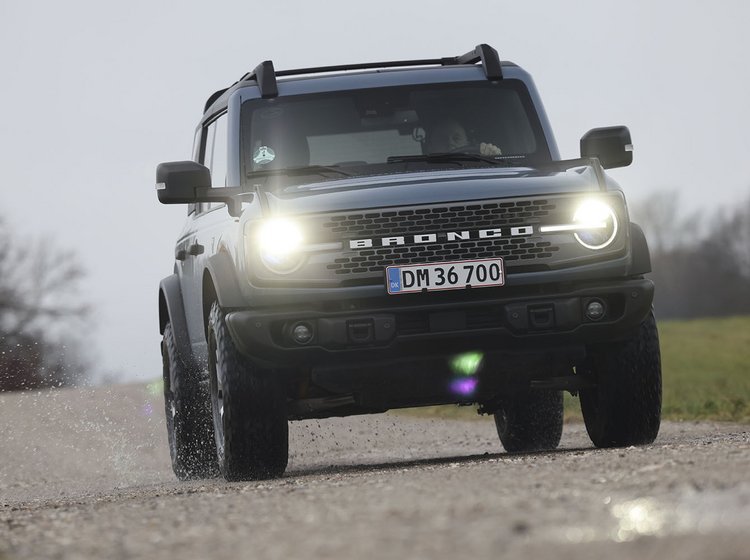 En Ford Bronco kører på en grusvej i tåge med forlygterne tændt