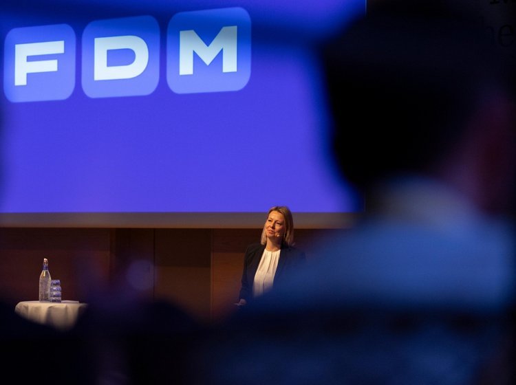 FDM Logo på blå baggrund. Administrerende direktør Stina Glavind taler til medarbejdere