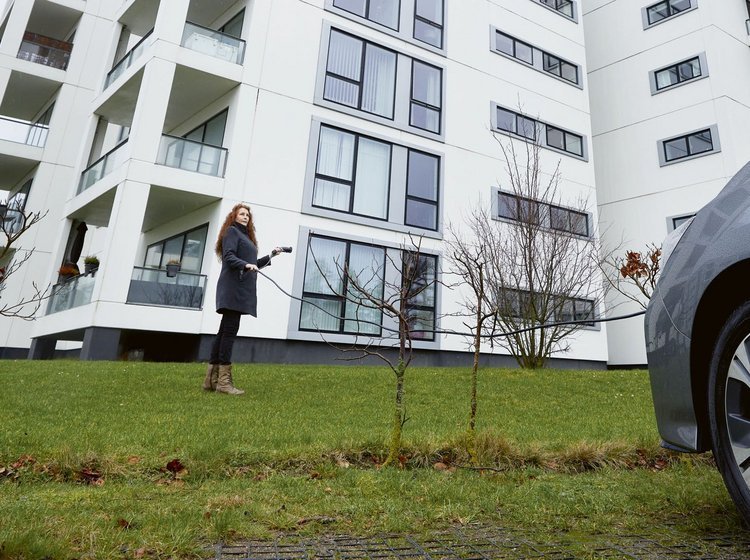 Kvinde med elbil og ladekabel foran boligblok