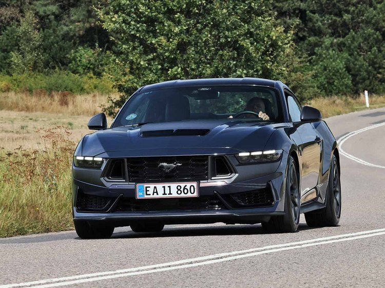 En sort Ford Mustang set forfra, kørende gennem en naturskøn rute.