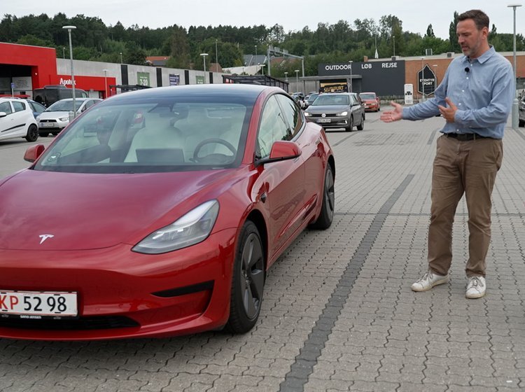 En mand og en dame kigger på en Rød Tesla Model 3