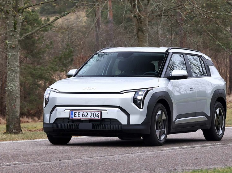 Kia EV3 set skråt forfra, mens den kører på vej mellem træer