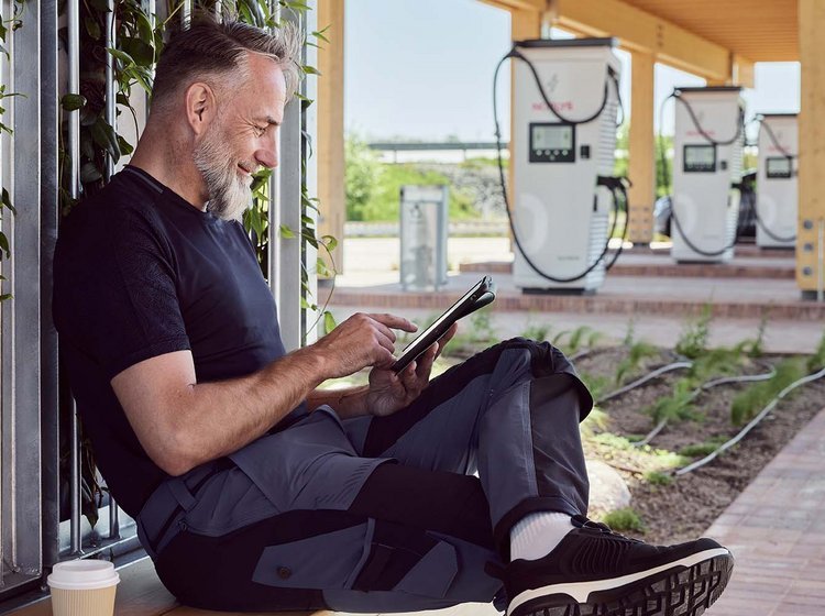 Mand sidder med kaffe og pc og venter på, at elbilen bliver ladet op