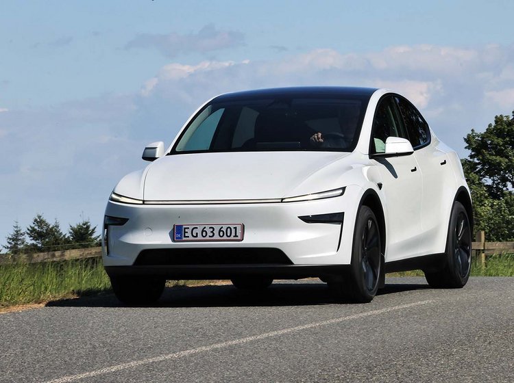 Tesla Model Y kører på en landevej med blå himmel i baggrunden