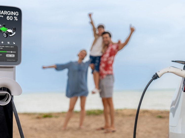Familie står på strand, mens elbil lades op i forgrunden