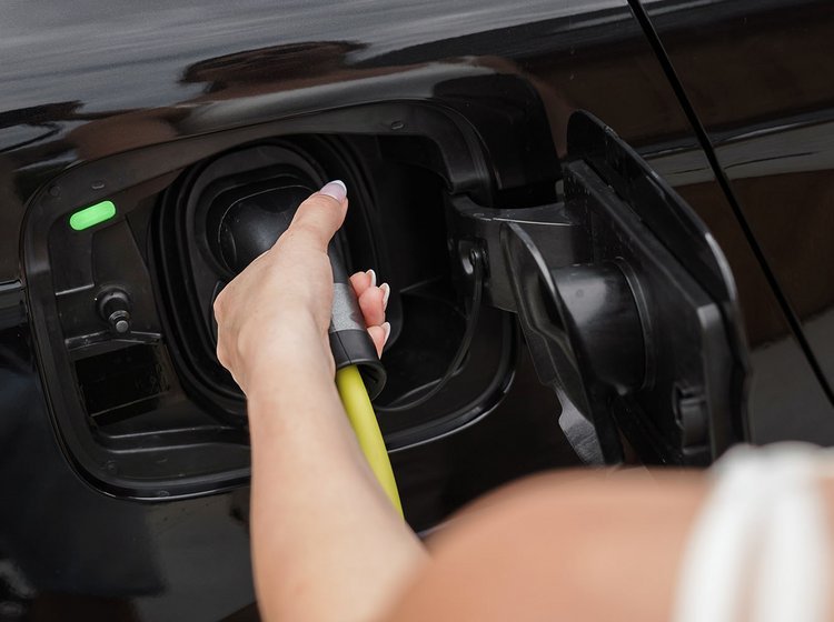 Kvinde sætter stik til opladning på en sort elbil