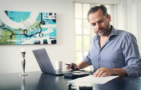 Mand sidder ved computer og kigger i en bunke papirer. 