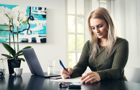 Kvinde sidder ved computer og kigger på papirer. 