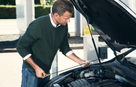 Mand har åbnet kølerhjelmen og er ved at tjekke olie på sin bil. 