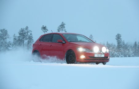 Rød bil kører på vej fyldt med sne. 