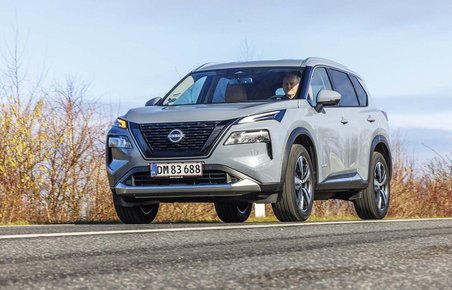 Nissan X-Trail kører på en vej med buskads i baggrunden