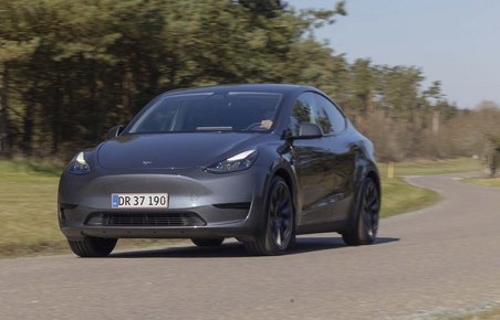 Tesla Model Y kører i sving på landevej med skov i baggrunden