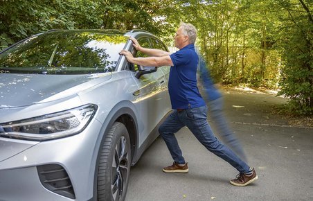 Fysioterapeut laver strækøvelser op ad en VW ID.4 med grønne træer i baggrunden