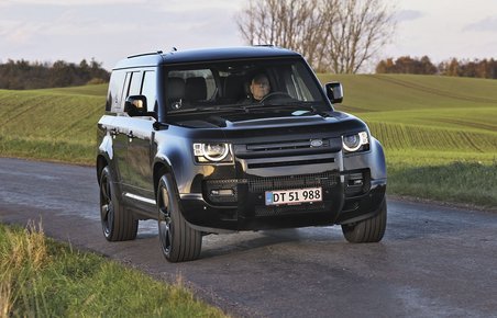 Land Rover Defender kører på en landevej med græs i baggrunden.