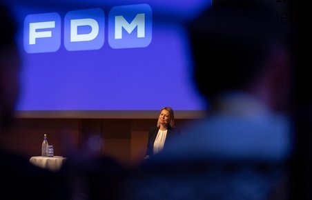 FDM Logo på blå baggrund. Administrerende direktør Stina Glavind taler til medarbejdere