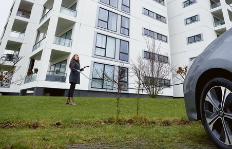 Kvinde med elbil og ladekabel foran boligblok